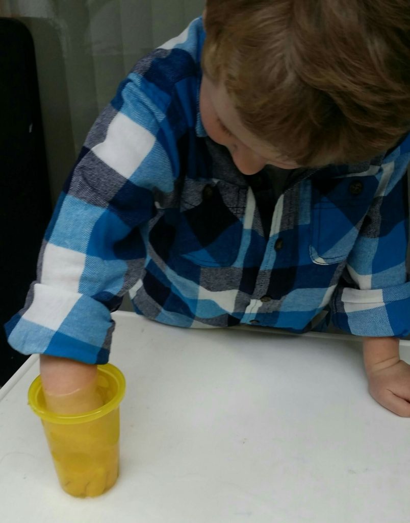 Preschooler discovers simple science principle of measuring volume through water displacement by putting his hand in a cup of water
