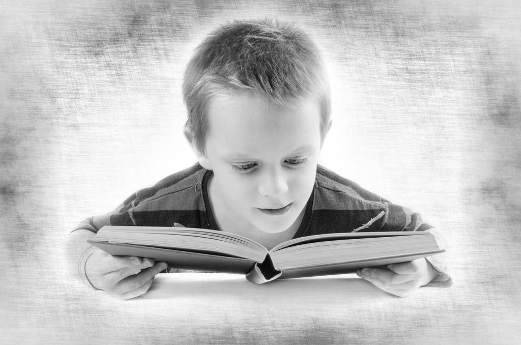young boy looking completely enthralled with the book that he's reading